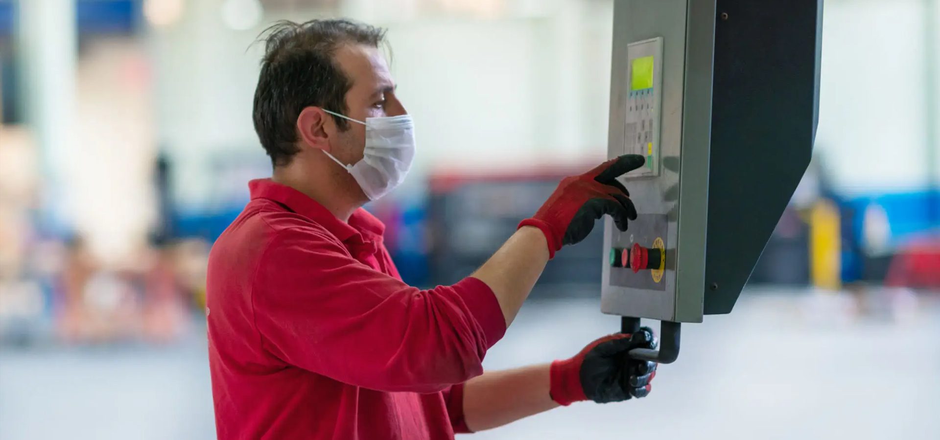 Worker in mask operating industrial control panel