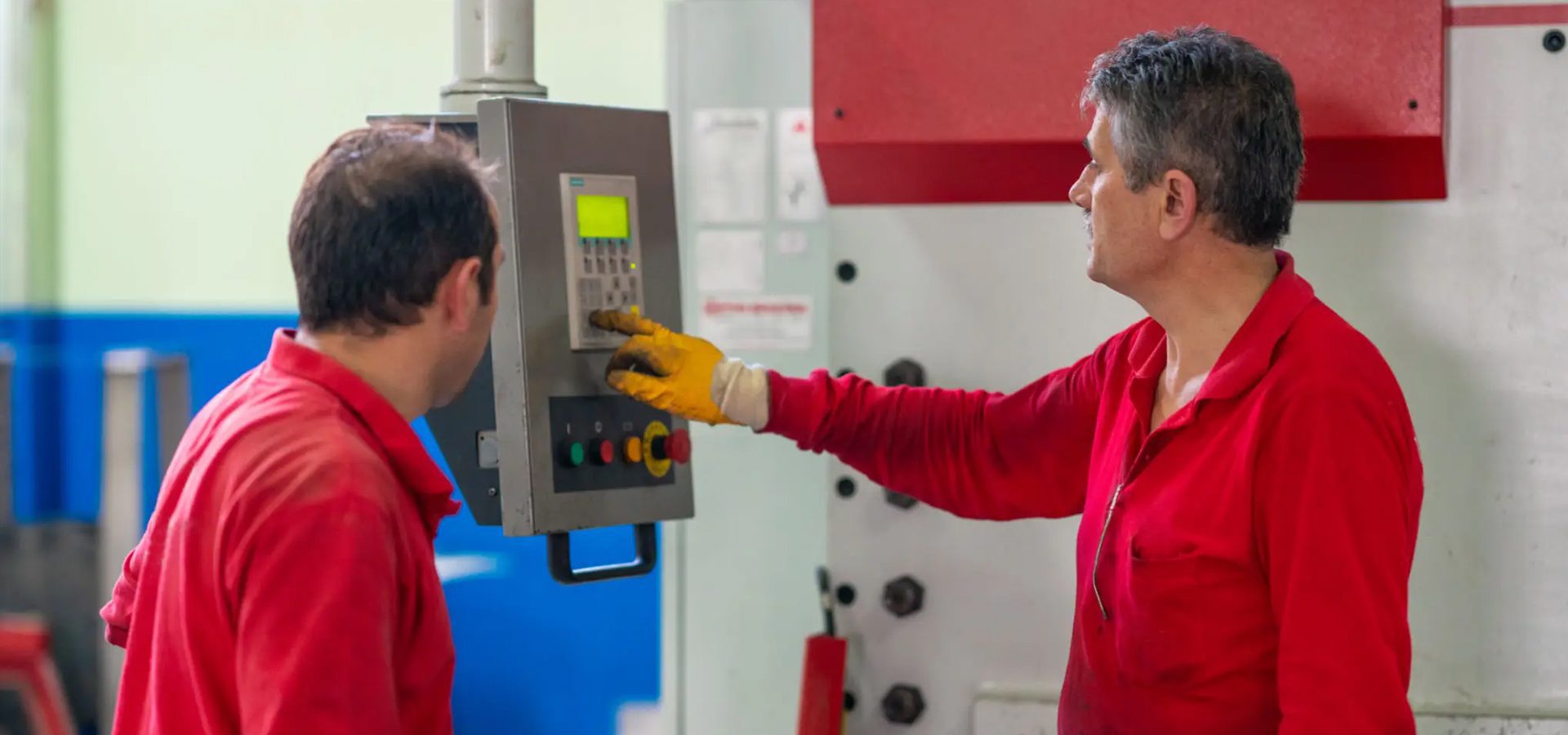 Two workers in red shirts using control panel